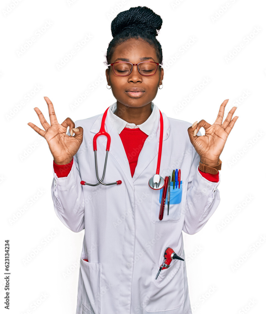 Young african american woman wearing doctor uniform and stethoscope relaxed and smiling with eyes closed doing meditation gesture with fingers. yoga concept. Young african american woman wearing doctor uniform and stethoscope relaxed and smiling with eyes closed doing meditation gesture with fingers. yoga concept.