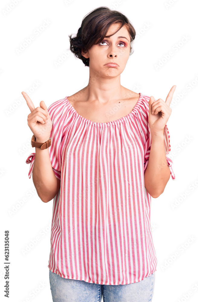 Beautiful young woman with short hair wearing casual summer clothes pointing up looking sad and upset, indicating direction with fingers, unhappy and depressed. Beautiful young woman with short hair wearing casual summer clothes pointing up looking sad and upset, indicating direction with fingers, unhappy and depressed.