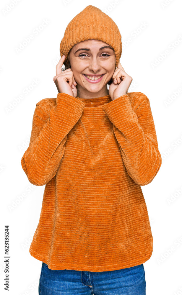 Young hispanic woman wearing casual clothes and wool cap covering ears with fingers with annoyed expression for the noise of loud music. deaf concept.