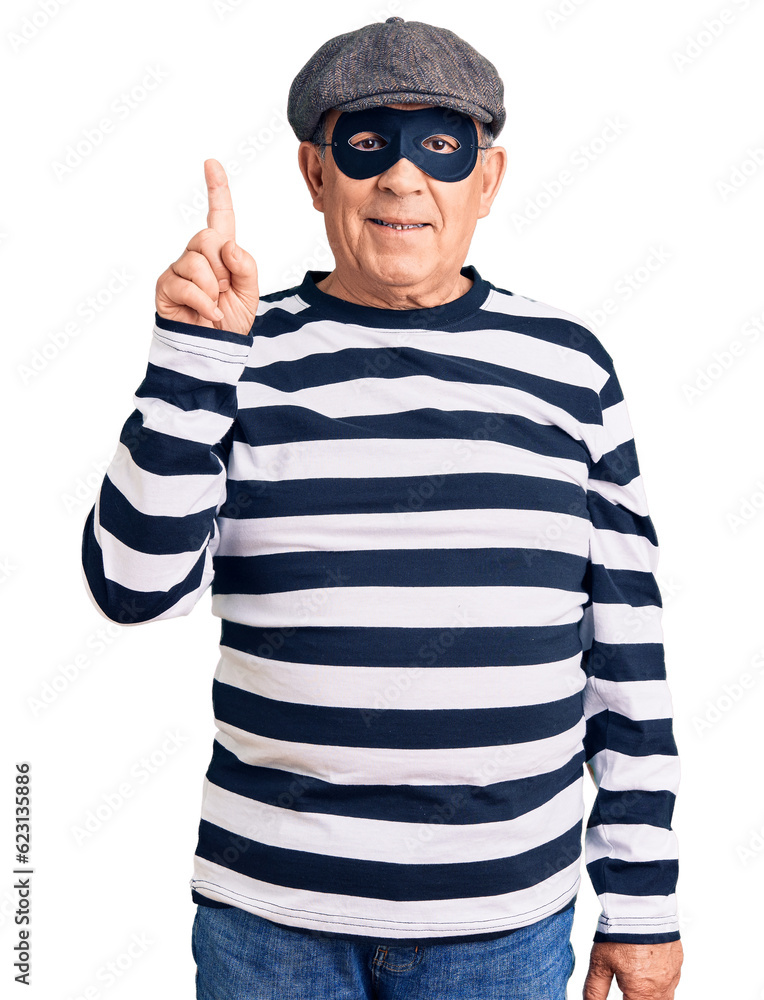 Senior handsome man wearing burglar mask and t-shirt pointing finger up with successful idea. exited and happy. number one. Senior handsome man wearing burglar mask and t-shirt pointing finger up with successful idea. exited and happy. number one.