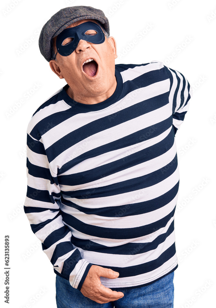 Senior handsome man wearing burglar mask and t-shirt suffering of backache, touching back with hand, muscular pain Senior handsome man wearing burglar mask and t-shirt suffering of backache, touching back with hand, muscular pain