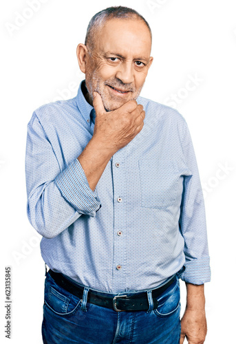 Senior man with grey hair and beard wearing casual blue shirt looking confident at the camera smiling with crossed arms and hand raised on chin. thinking positive. © Krakenimages.com