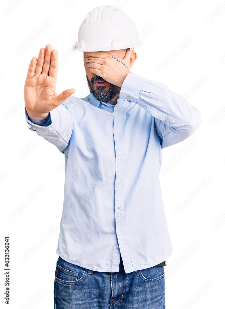 Young handsome man wearing architect hardhat covering eyes with hands and doing stop gesture with sad and fear expression. embarrassed and negative concept. Young handsome man wearing architect hardhat covering eyes with hands and doing stop gesture with sad and fear expression. embarrassed and negative concept.