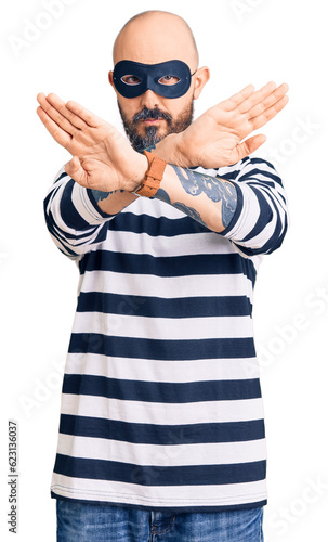 Young handsome man wearing burglar mask rejection expression crossing arms and palms doing negative sign, angry face