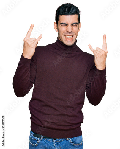 Handsome hispanic man wearing casual turtleneck sweater shouting with crazy expression doing rock symbol with hands up. music star. heavy concept.