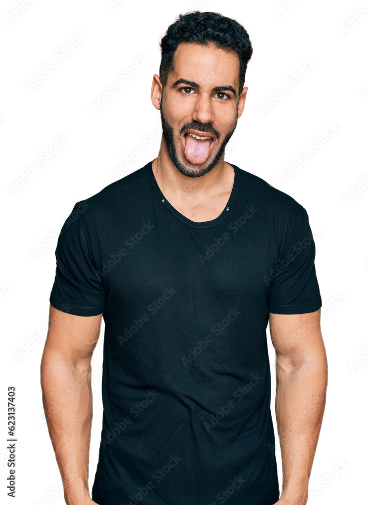 Hispanic man with beard wearing casual black t shirt sticking tongue out happy with funny expression. emotion concept. Hispanic man with beard wearing casual black t shirt sticking tongue out happy with funny expression. emotion concept.