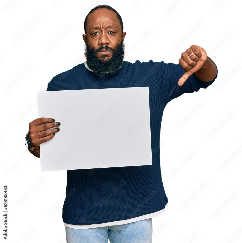 Young african american man holding blank empty banner with angry face, negative sign showing dislike with thumbs down, rejection concept Young african american man holding blank empty banner with angry face, negative sign showing dislike with thumbs down, rejection concept