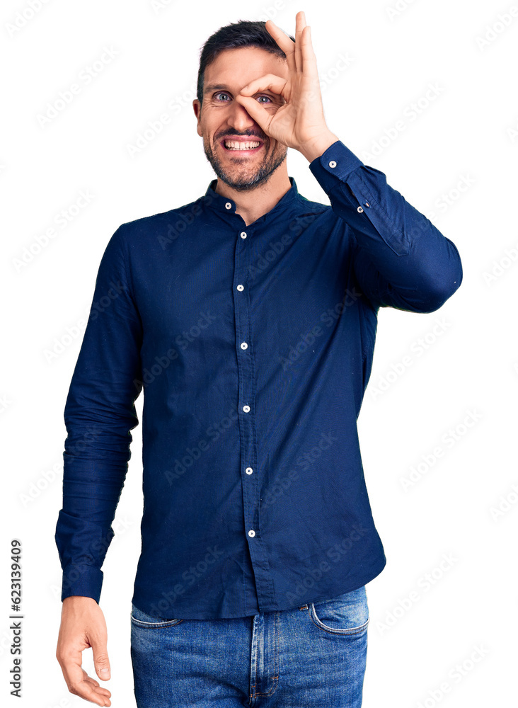 Young handsome man wearing casual shirt doing ok gesture with hand smiling, eye looking through fingers with happy face. Young handsome man wearing casual shirt doing ok gesture with hand smiling, eye looking through fingers with happy face.