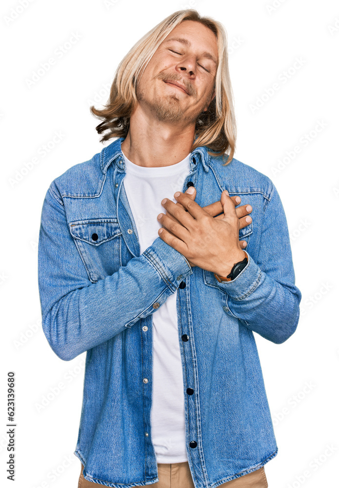 Caucasian man with blond long hair wearing casual denim jacket smiling with hands on chest with closed eyes and grateful gesture on face. health concept.