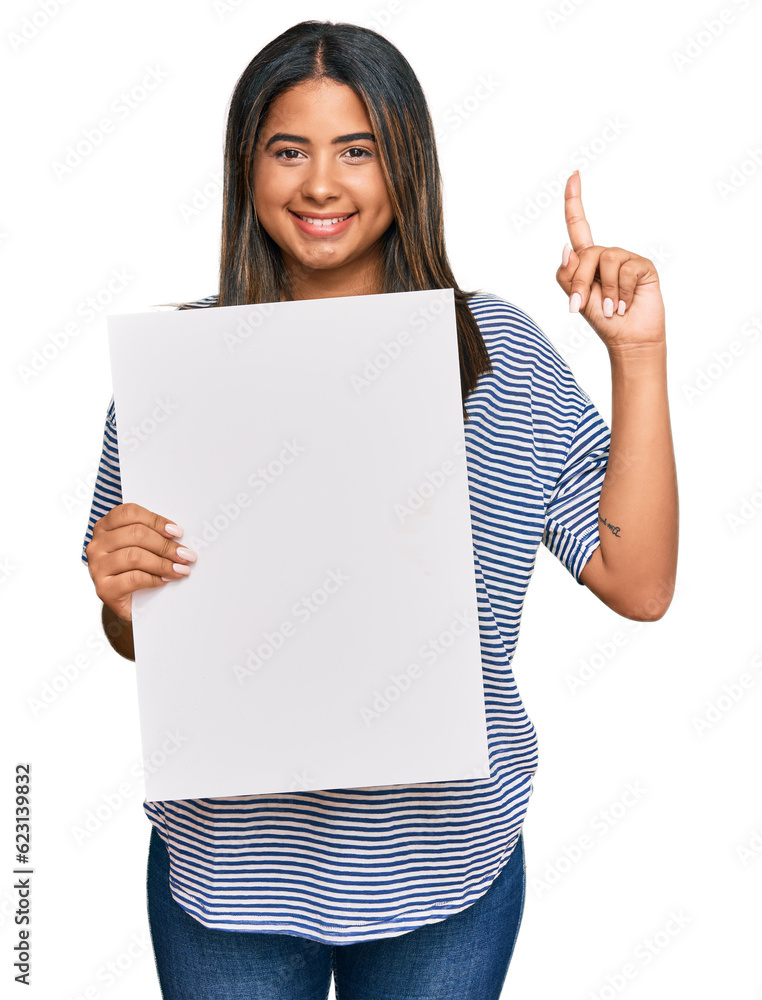 Young latin girl holding blank empty banner surprised with an idea or question pointing finger with happy face, number one Young latin girl holding blank empty banner surprised with an idea or question pointing finger with happy face, number one