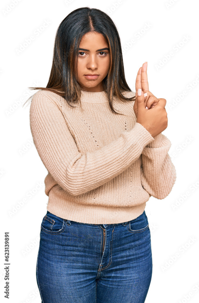Young latin girl wearing wool winter sweater holding symbolic gun with hand gesture, playing killing shooting weapons, angry face Young latin girl wearing wool winter sweater holding symbolic gun with hand gesture, playing killing shooting weapons, angry face