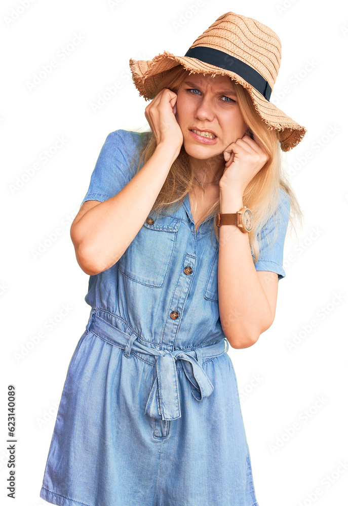 Young beautiful blonde woman wearing summer hat and dress covering ears with fingers with annoyed expression for the noise of loud music. deaf concept. Young beautiful blonde woman wearing summer hat and dress covering ears with fingers with annoyed expression for the noise of loud music. deaf concept.