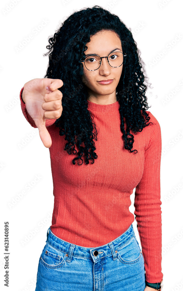 Young hispanic woman with curly hair wearing glasses looking unhappy and angry showing rejection and negative with thumbs down gesture. bad expression. Young hispanic woman with curly hair wearing glasses looking unhappy and angry showing rejection and negative with thumbs down gesture. bad expression.