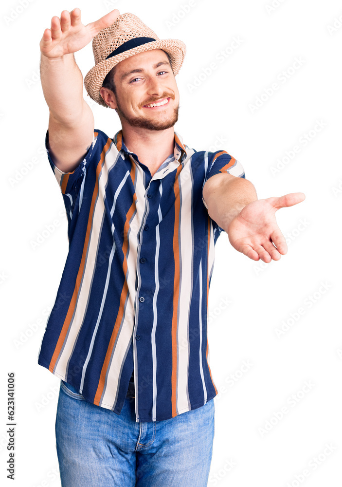 Young handsome caucasian man wearing summer hat looking at the camera smiling with open arms for hug. cheerful expression embracing happiness. Young handsome caucasian man wearing summer hat looking at the camera smiling with open arms for hug. cheerful expression embracing happiness.