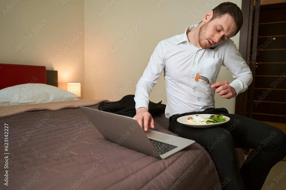 Serious businessman calling on smartphone during lunch in hotel suite Serious businessman calling on smartphone during lunch in hotel suite