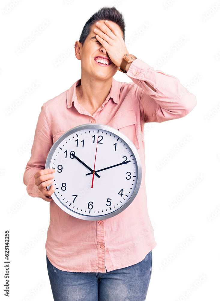 Young woman with short hair holding big clock stressed and frustrated with hand on head, surprised and angry face Young woman with short hair holding big clock stressed and frustrated with hand on head, surprised and angry face