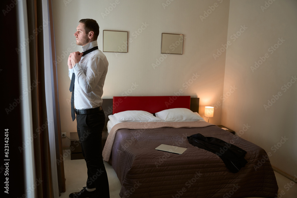 Thoughtful young gentleman getting dressed for business meeting in aparthotel