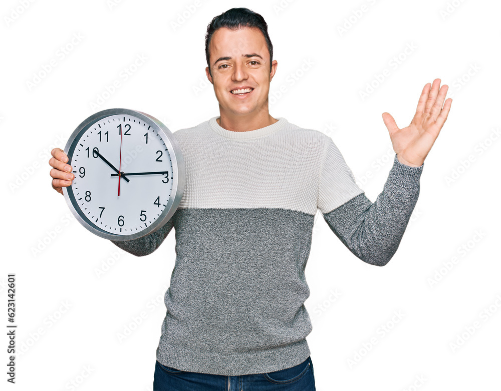 Handsome young man holding big clock celebrating victory with happy smile and winner expression with raised hands Handsome young man holding big clock celebrating victory with happy smile and winner expression with raised hands