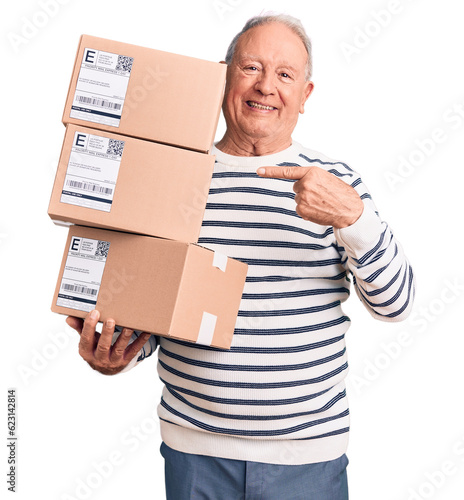 Senior handsome grey-haired man holding delivery boxes smiling happy pointing with hand and finger