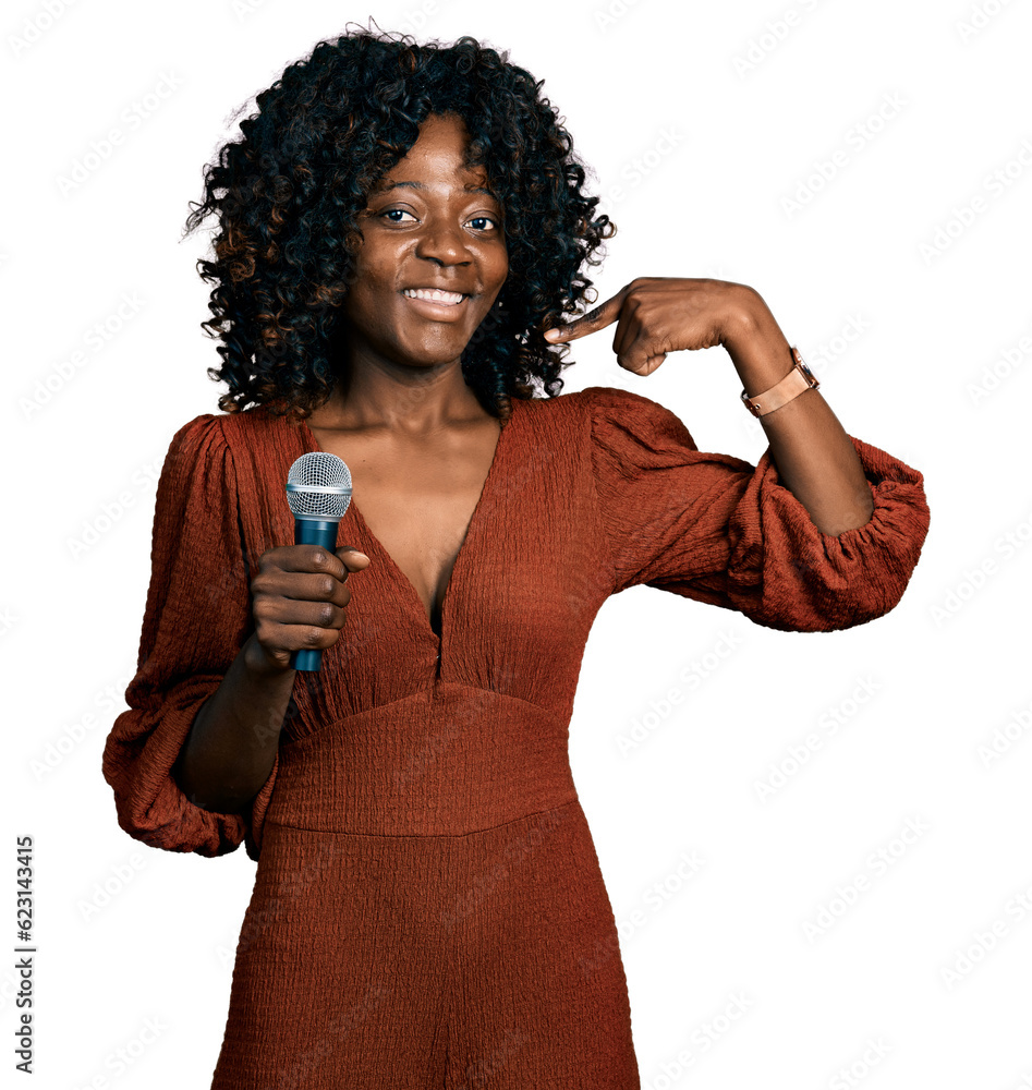 African woman with curly hair singing song using microphone looking confident with smile on face, pointing oneself with fingers proud and happy. African woman with curly hair singing song using microphone looking confident with smile on face, pointing oneself with fingers proud and happy.