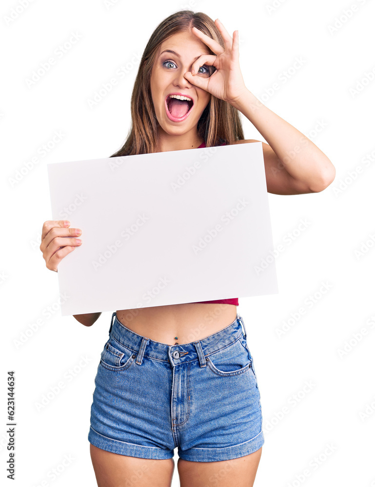 Young beautiful blonde woman holding blank empty banner smiling happy doing ok sign with hand on eye looking through fingers Young beautiful blonde woman holding blank empty banner smiling happy doing ok sign with hand on eye looking through fingers