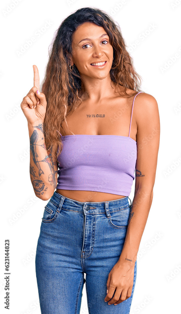 Young hispanic woman with tattoo wearing casual clothes pointing finger up with successful idea. exited and happy. number one. Young hispanic woman with tattoo wearing casual clothes pointing finger up with successful idea. exited and happy. number one.
