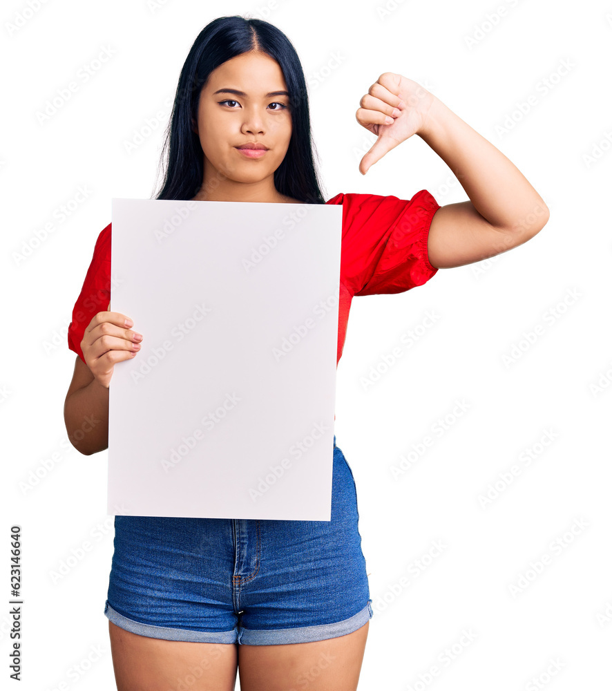 Young beautiful asian girl holding blank empty banner with angry face, negative sign showing dislike with thumbs down, rejection concept Young beautiful asian girl holding blank empty banner with angry face, negative sign showing dislike with thumbs down, rejection concept