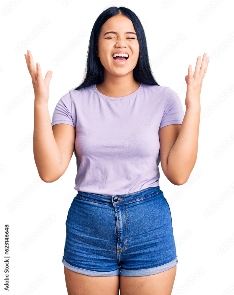 Young beautiful asian girl wearing casual clothes celebrating mad and crazy for success with arms raised and closed eyes screaming excited. winner concept Young beautiful asian girl wearing casual clothes celebrating mad and crazy for success with arms raised and closed eyes screaming excited. winner concept