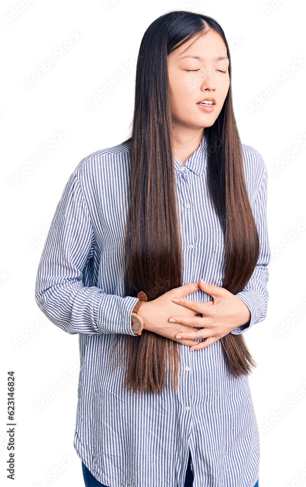 Young beautiful chinese woman wearing casual shirt with hand on stomach because nausea, painful disease feeling unwell. ache concept. Young beautiful chinese woman wearing casual shirt with hand on stomach because nausea, painful disease feeling unwell. ache concept.