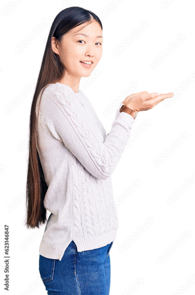 Young beautiful chinese woman wearing casual sweater pointing aside with hands open palms showing copy space, presenting advertisement smiling excited happy Young beautiful chinese woman wearing casual sweater pointing aside with hands open palms showing copy space, presenting advertisement smiling excited happy