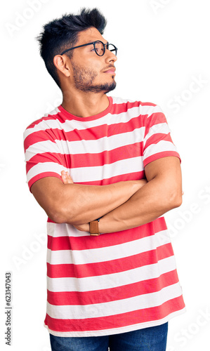 Handsome latin american young man wearing casual clothes and glasses looking to the side with arms crossed convinced and confident