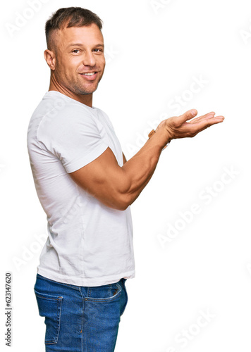 Handsome muscle man wearing casual white tshirt pointing aside with hands open palms showing copy space, presenting advertisement smiling excited happy