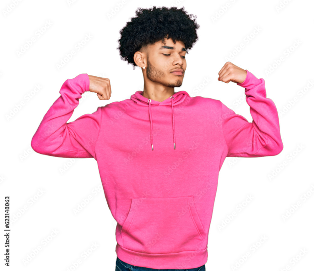 Young african american man with afro hair wearing casual pink sweatshirt showing arms muscles smiling proud. fitness concept. Young african american man with afro hair wearing casual pink sweatshirt showing arms muscles smiling proud. fitness concept.