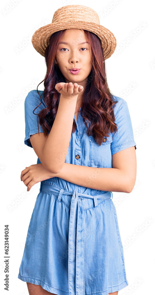 Young beautiful chinese girl wearing summer hat looking at the camera blowing a kiss with hand on air being lovely and sexy. love expression. Young beautiful chinese girl wearing summer hat looking at the camera blowing a kiss with hand on air being lovely and sexy. love expression.
