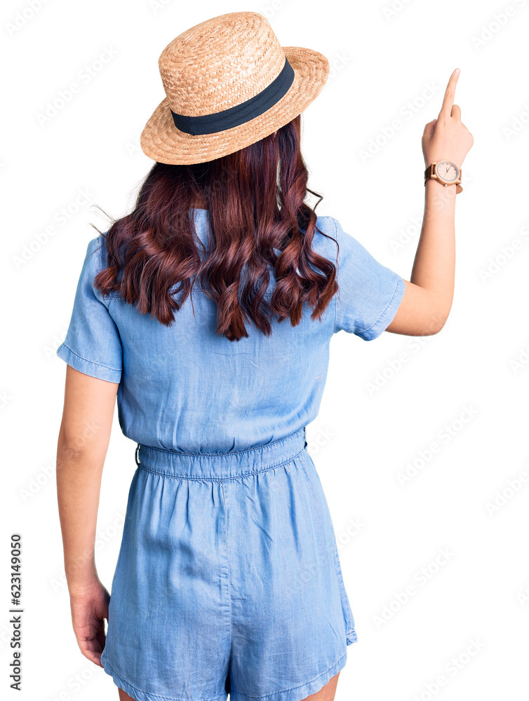 Young beautiful chinese girl wearing summer hat posing backwards pointing ahead with finger hand