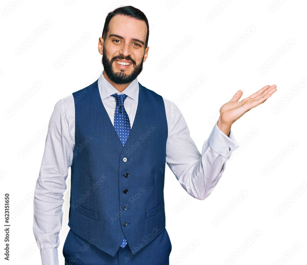 Young man with beard wearing business vest smiling cheerful presenting and pointing with palm of hand looking at the camera. Young man with beard wearing business vest smiling cheerful presenting and pointing with palm of hand looking at the camera.