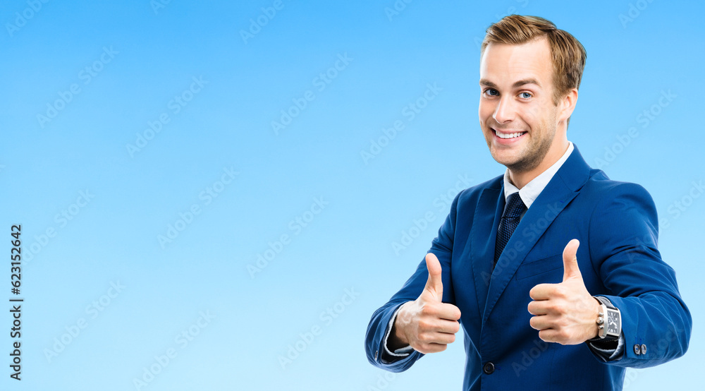 Fototapeta premium Portrait of confident businessman showing thumbs up hand sign gesture, on blue background. Business success concept. Young happy smiling man at studio.