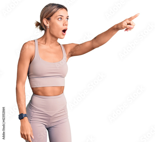 Beautiful caucasian woman wearing sportswear pointing with finger surprised ahead, open mouth amazed expression, something on the front © Krakenimages.com