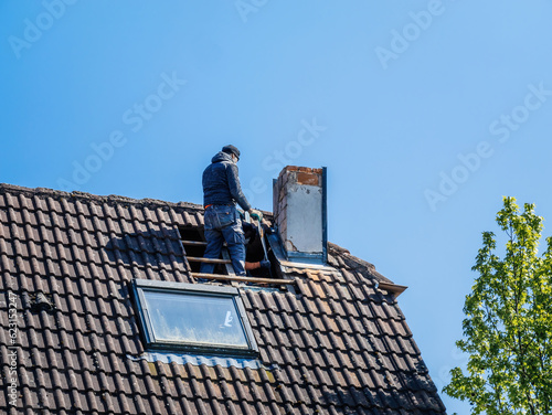 A team of roofers working on a building rooftop exterior, repairing and insulating the chimney under a clear sky