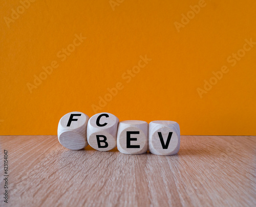 Battery Electric Vehicle (BEV) or a Fuel Cell Electric Vehicle (FCEV) symbol. Turned wooden cubes and changes the word FCEV to BEV on a beautiful wooden table, orange background. Copy space