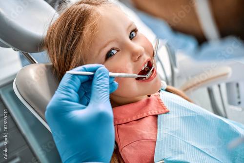 Children's dentistry. Close-up portrait of a girl sitting in a dental chair and having her teeth treated. A doctor in gloves holds instruments.