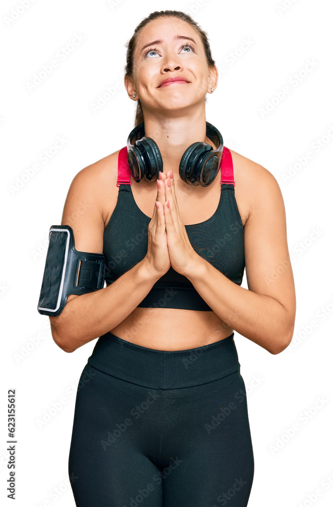Beautiful blonde woman wearing gym clothes and using headphones begging and praying with hands together with hope expression on face very emotional and worried. begging. Beautiful blonde woman wearing gym clothes and using headphones begging and praying with hands together with hope expression on face very emotional and worried. begging.