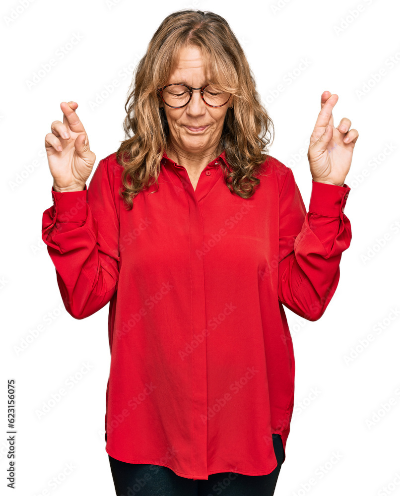 Middle age blonde woman wearing casual shirt over red background gesturing finger crossed smiling with hope and eyes closed. luck and superstitious concept. Middle age blonde woman wearing casual shirt over red background gesturing finger crossed smiling with hope and eyes closed. luck and superstitious concept.