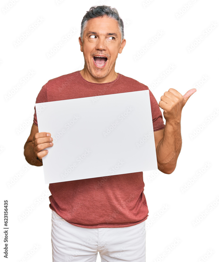 Handsome middle age man holding blank empty banner pointing thumb up to the side smiling happy with open mouth Handsome middle age man holding blank empty banner pointing thumb up to the side smiling happy with open mouth
