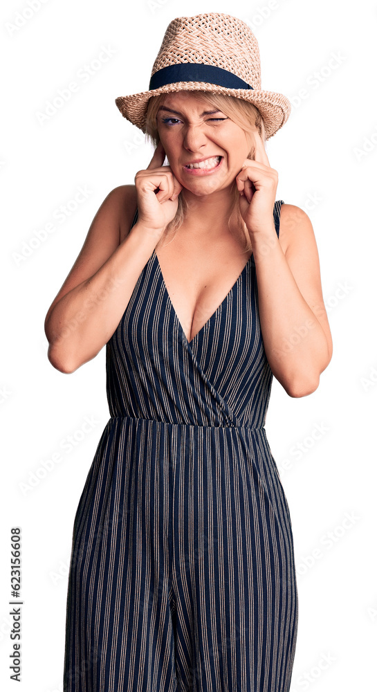 Young beautiful blonde woman wearing summer hat and dress covering ears with fingers with annoyed expression for the noise of loud music. deaf concept. Young beautiful blonde woman wearing summer hat and dress covering ears with fingers with annoyed expression for the noise of loud music. deaf concept.