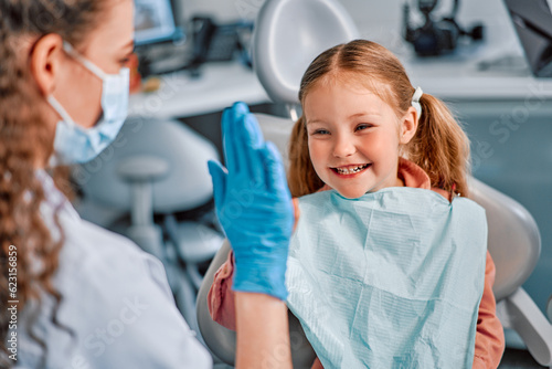 Children s dentistry. The child sits in the dental chair and cheerfully gives a high five to the nurse.