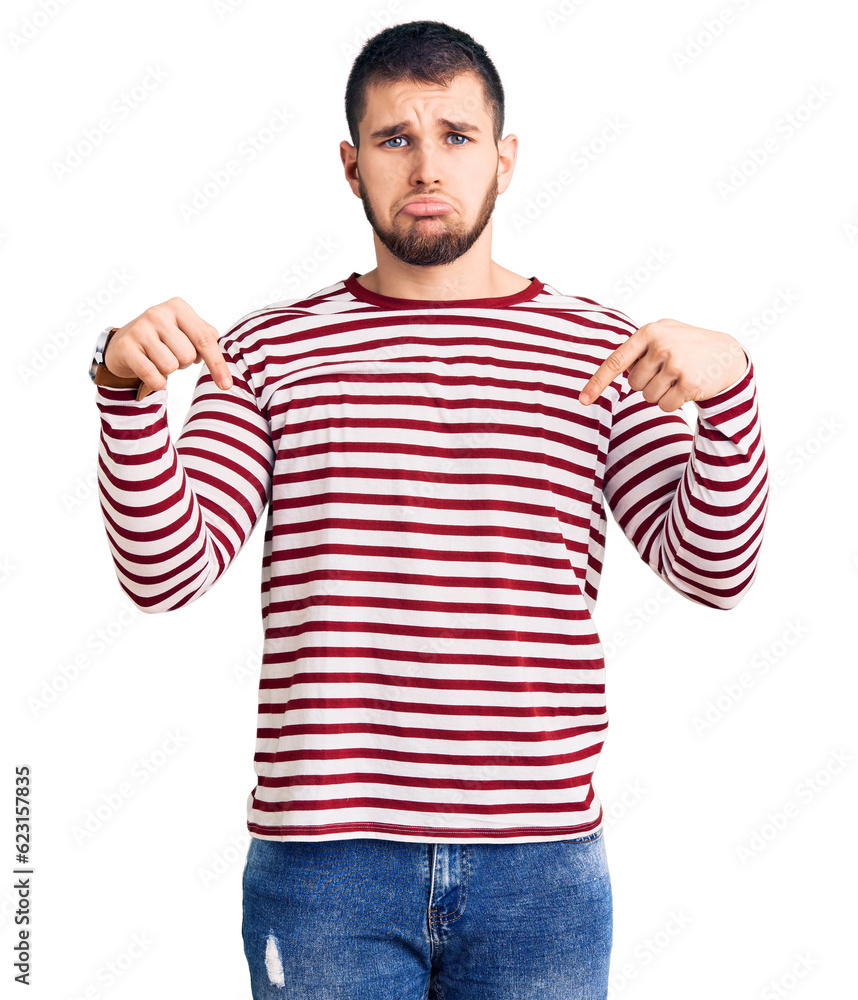 Young handsome man wearing striped sweater pointing down looking sad and upset, indicating direction with fingers, unhappy and depressed. Young handsome man wearing striped sweater pointing down looking sad and upset, indicating direction with fingers, unhappy and depressed.