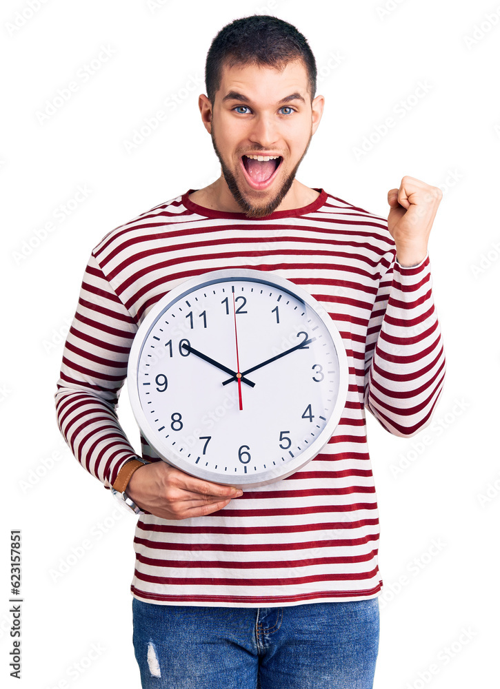 Young handsome man holding big clock screaming proud, celebrating victory and success very excited with raised arms Young handsome man holding big clock screaming proud, celebrating victory and success very excited with raised arms