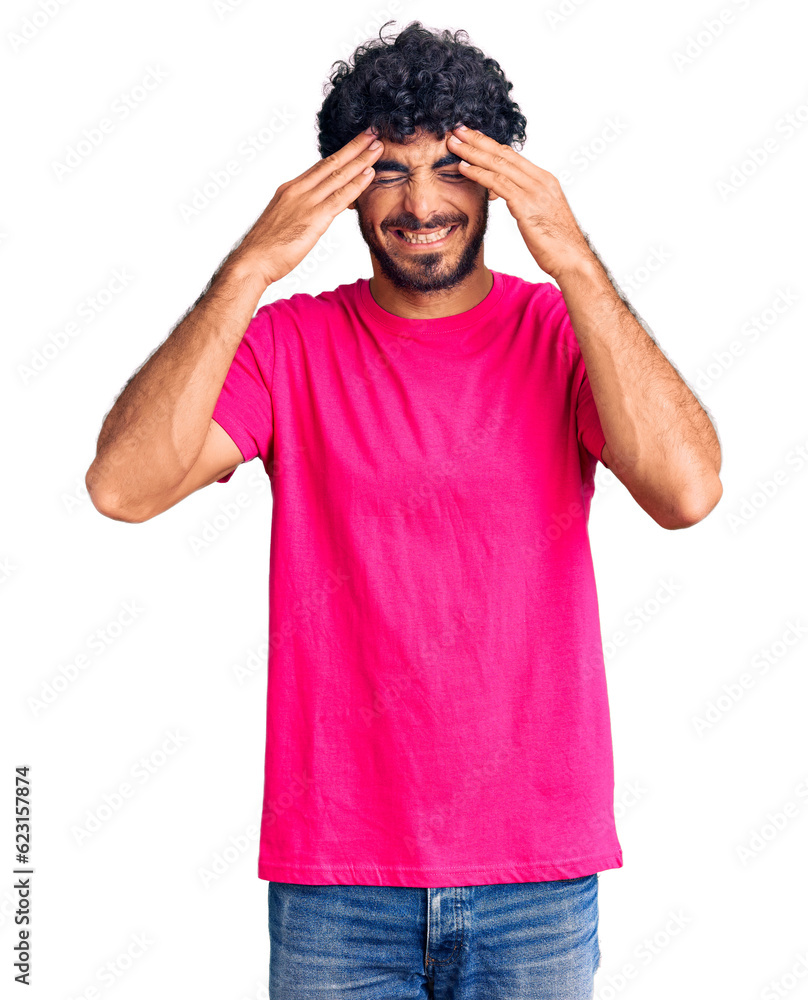 Handsome young man with curly hair and bear wearing casual pink tshirt with hand on head for pain in head because stress. suffering migraine. Handsome young man with curly hair and bear wearing casual pink tshirt with hand on head for pain in head because stress. suffering migraine.