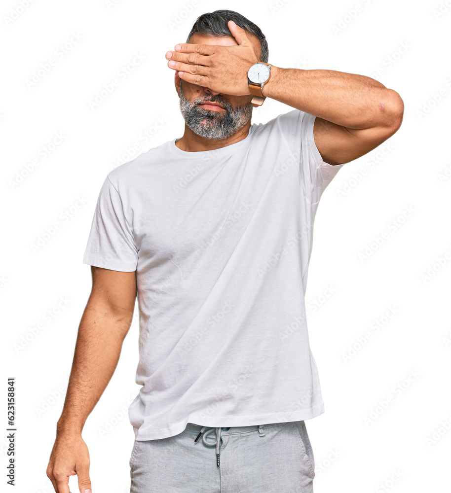 Middle age handsome man wearing casual white tshirt covering eyes with hand, looking serious and sad. sightless, hiding and rejection concept Middle age handsome man wearing casual white tshirt covering eyes with hand, looking serious and sad. sightless, hiding and rejection concept